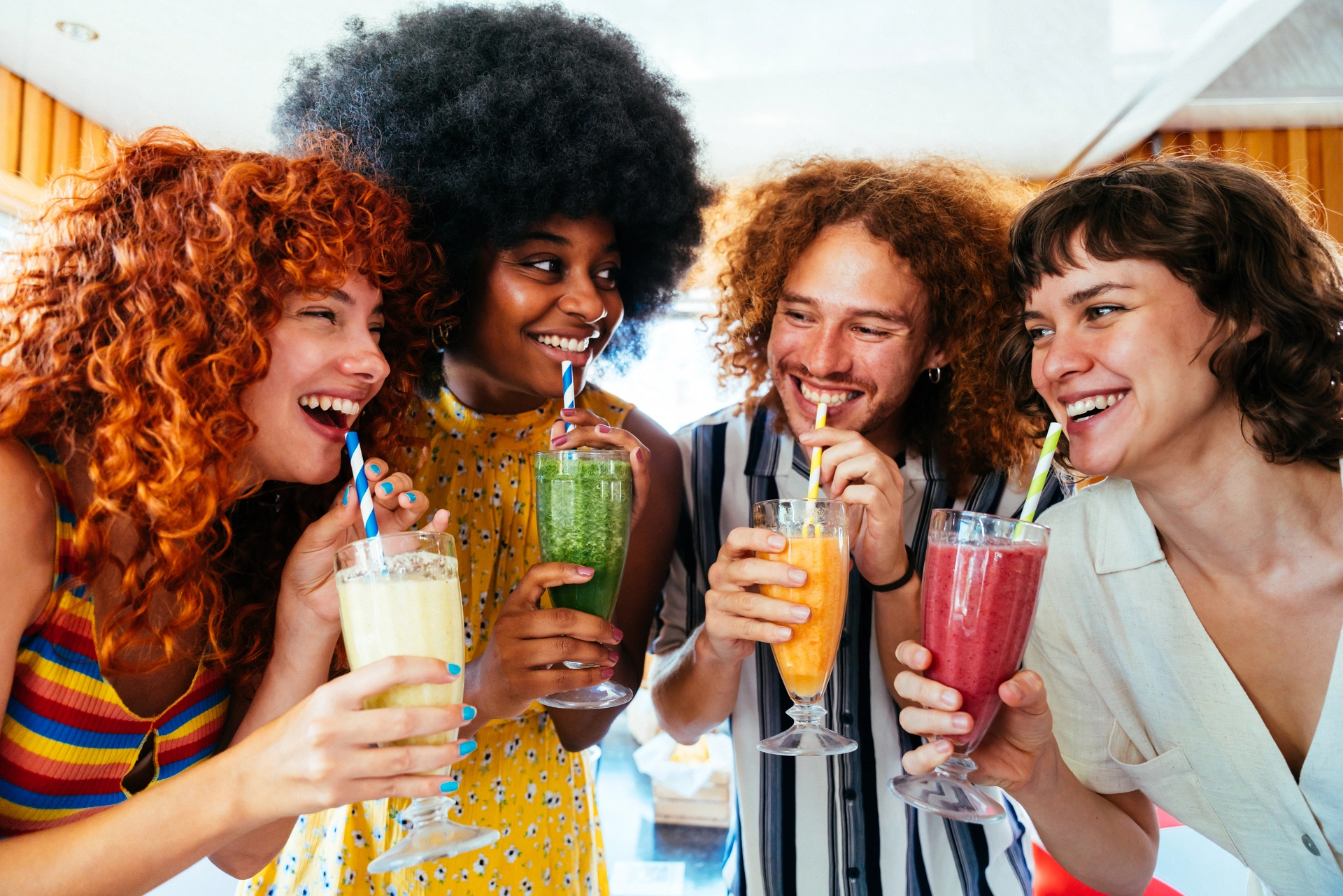 A group of friends joyfully sipping smoothies together, all smiling and enjoying their time outdoors.